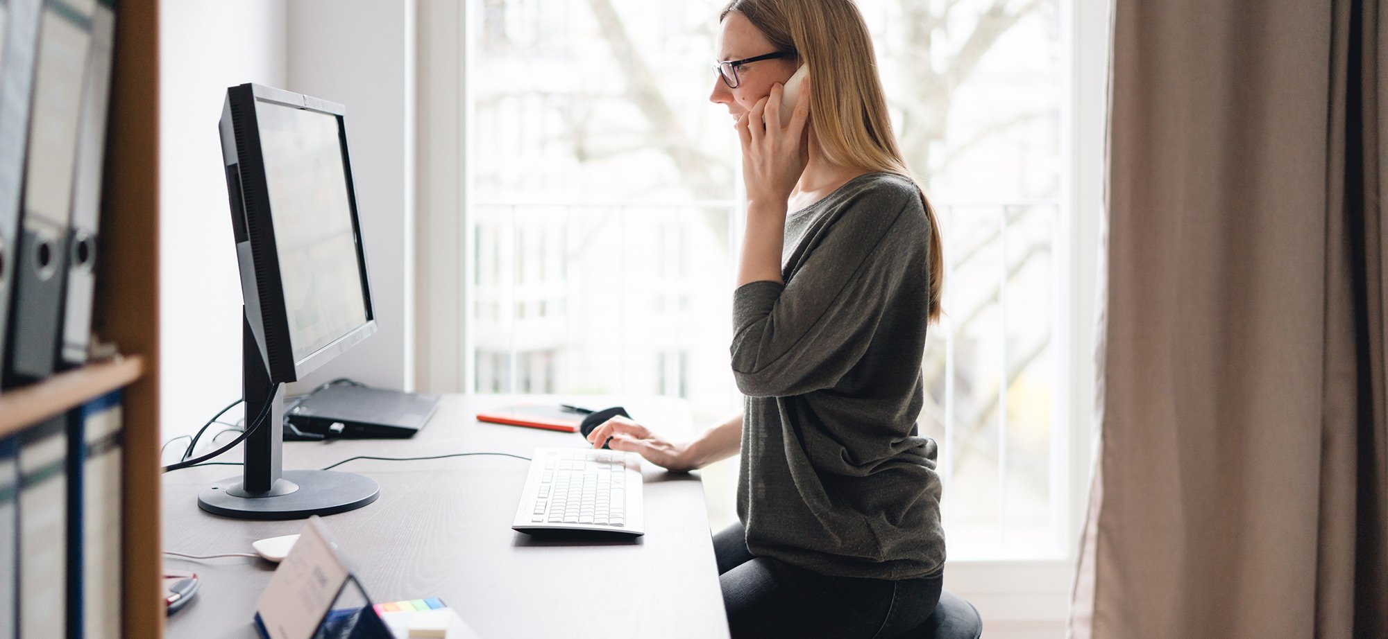 Frau, die an einem Bildschirm-Arbeitsplatz sitzt und telefoniert