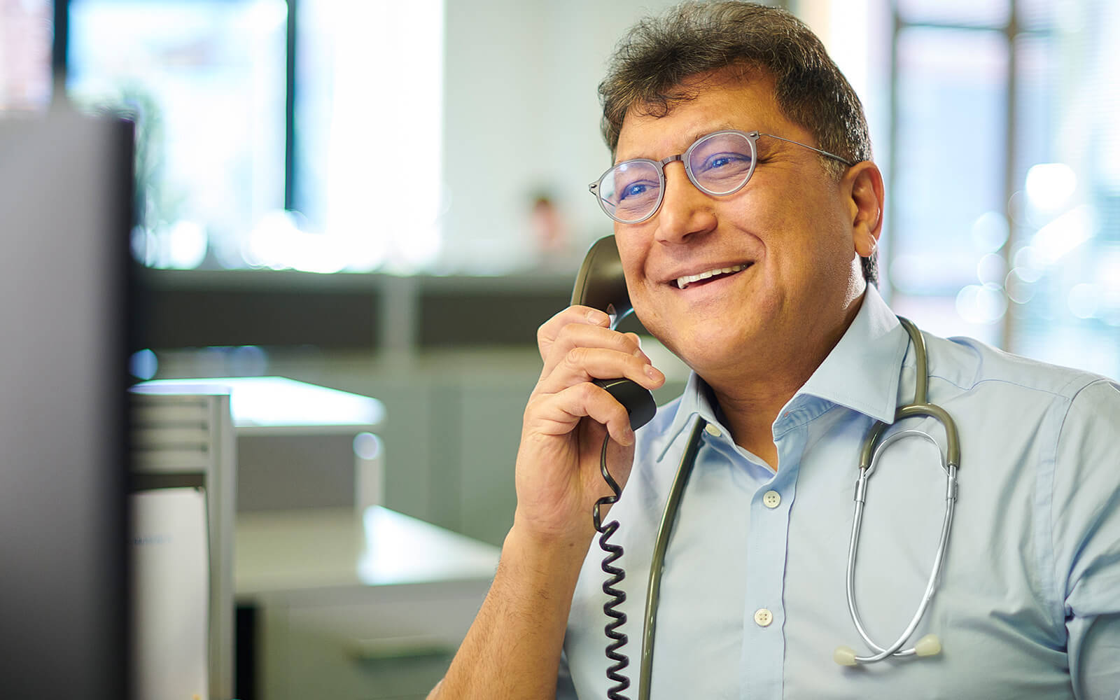 Arzt mit Stethoskop telefoniert im Büro – Symbolbild für die Telefon-Sprechstunde mit dem Betriebsarzt zur schnellen Unterstützung
