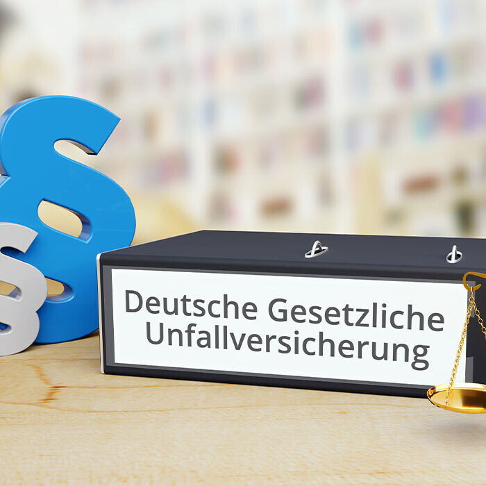 Ordner mit Beschriftung "Deutsche Gesetzliche Unfallversicherung", daneben stehen Paragrafen und eine Waage