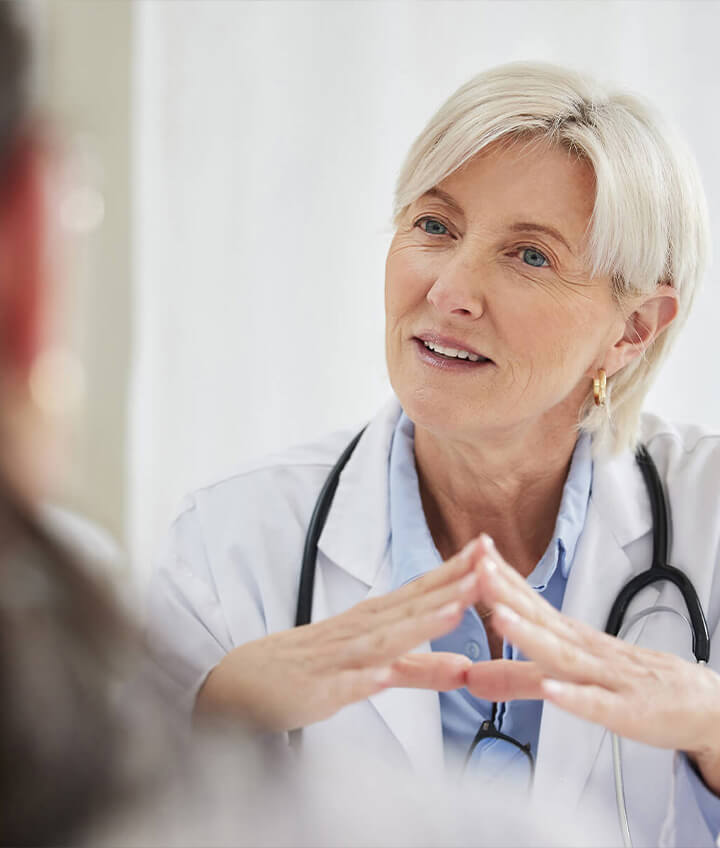 Eine Ärztin im weißen Kittel mit Stethoskop, die während einer Sprechstunde aufmerksam zuhört und mit einem Patienten spricht.